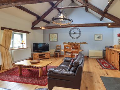 A living room with wooden beams a leather sofa a wooden coffee table a television and a dining area at Tullythwaite Garth in Crosthwaite