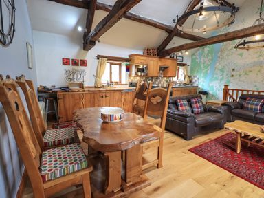 A rustic kitchen and living area with wooden dining table and chairs leather sofas and a large wall map at Tullythwaite Garth in Crosthwaite