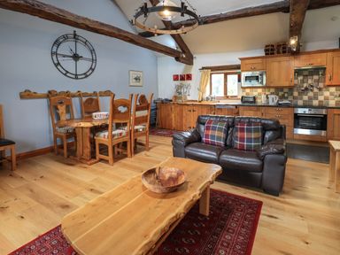 A kitchen and dining area with wooden furniture a leather sofa and exposed ceiling beams at Tullythwaite Garth in Crosthwaite