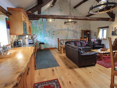 A living room with brown leather sofas a wooden coffee table and a kitchen area with wooden cabinets and countertops at Tullythwaite Garth in Crosthwaite