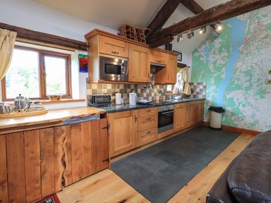 A kitchen with wooden cabinets a microwave oven black countertop tiled backsplash and a large map on the wall at Tullythwaite Garth in Crosthwaite