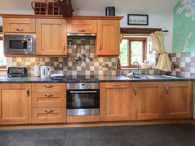 A kitchen with wooden cabinets a built-in oven microwave toaster kettle utensils hanging and a sink under a window at Tullythwaite Garth in Crosthwaite