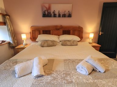 A bedroom with a wooden bed headboard bedside tables with lamps and rolled towels on the bed at Tullythwaite Garth in Crosthwaite