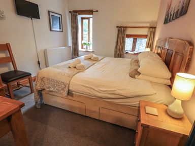 A bedroom with a double bed two windows a wooden chair a wooden nightstand with a lamp and a wall-mounted television at Tullythwaite Garth in Crosthwaite