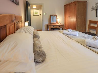 A bedroom with a bed pillows a wooden wardrobe a dressing table with lamp and chair at Tullythwaite Garth in Crosthwaite