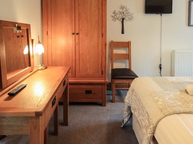 A bedroom with wooden wardrobe dressing table chair wall decoration and a bed at Tullythwaite Garth in Crosthwaite