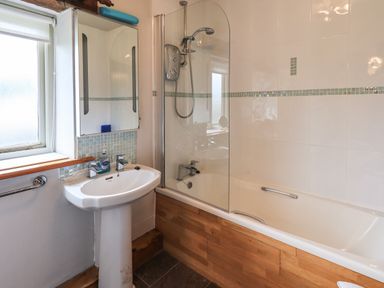 A bathroom with a pedestal sink a mirrored cabinet shower and bathtub with wood paneling at Tullythwaite Garth in Crosthwaite