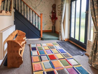 An entryway with a wooden bench colorful square patterned rug stairs and glass paneled door at Tullythwaite Garth in Crosthwaite