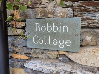 A stone wall with a metal sign that reads Bobbin Cottage at Bobbin Cottage in Ings