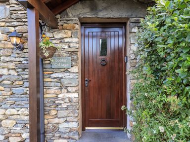 A wooden door with a knocker and small window in a stone wall with a hanging flower basket lamp and greenery at Bobbin Cottage in Ings