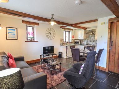 A living room with sofa red cushions armchair and dining table with kitchen in the background at Bobbin Cottage in Ings