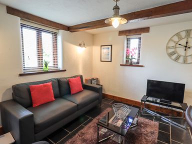 A living room with a black sofa with red cushions a glass coffee table a television and a wall clock at Bobbin Cottage in Ings