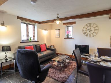 A living room with black sofa and red cushions next to armchair and dining table at Bobbin Cottage in Ings