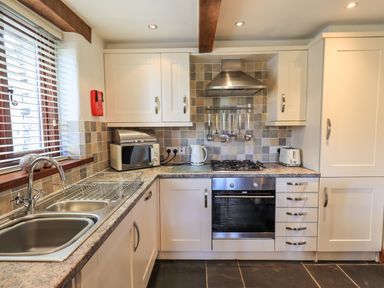 A kitchen with a sink dish rack microwave oven kettle toaster and hanging utensils at Bobbin Cottage in Ings