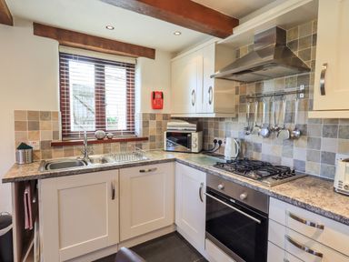 A kitchen with a sink under a window a gas stove an oven microwave and kitchen utensils at Bobbin Cottage in Ings
