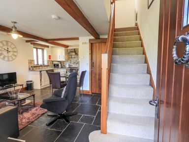 A living room with a black armchair a dining table with chairs a kitchen area and a carpeted staircase at Bobbin Cottage in Ings