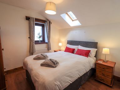 A bedroom with a double bed with red cushions two bedside tables with lamps a window with curtains and a skylight at Bobbin Cottage in Ings