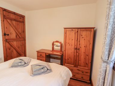 A bedroom with a wooden wardrobe and dressing table next to a wooden door at Bobbin Cottage in Ings