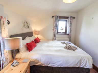 A bedroom with a bed with white linens and red pillows two bedside lamps and a window with floral curtains at Bobbin Cottage in Ings