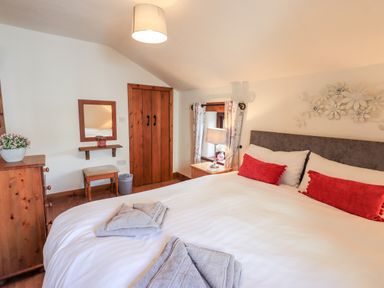 A bedroom with a double bed white bedding and red cushions bedside table with lamp wooden chest of drawers and closet at Bobbin Cottage in Ings