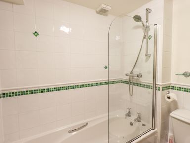 A bathroom with a bathtub shower combination and white tiled walls with green accents at Bobbin Cottage in Ings