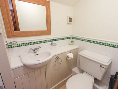 A small bathroom with a sink and toilet with a wooden mirror and green tile border at Bobbin Cottage in Ings