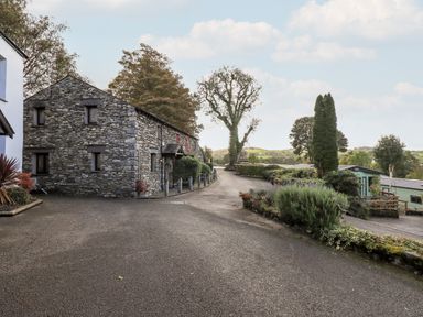 An outdoor area with a stone building on the left a paved driveway trees and shrubs at Bobbin Cottage in Ings