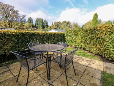 An outdoor patio area with a round metal table and four metal chairs surrounded by hedges at Bobbin Cottage in Ings