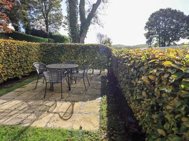 A patio area with a round metal table and four chairs surrounded by hedges at Bobbin Cottage in Ings
