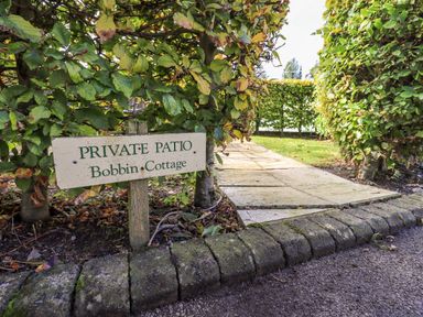A private patio sign by a paved path surrounded by trimmed hedges at Bobbin Cottage in Ings