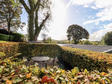 An outdoor patio with a round metal table and four chairs surrounded by hedges and trees at Bobbin Cottage in Ings