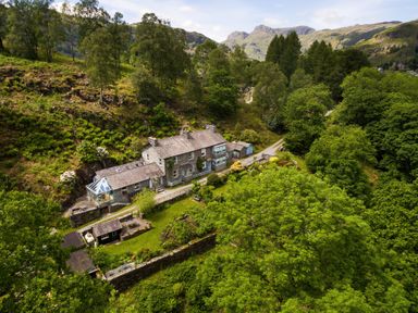 A stone house with a garden surrounded by trees and hills at The Stable At Oakbank in Elterwater