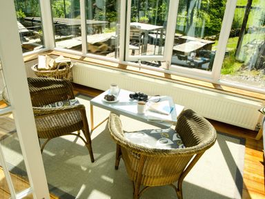 A sunroom with wicker chairs a table with coffee mugs books and binoculars at The Stable At Oakbank in Elterwater