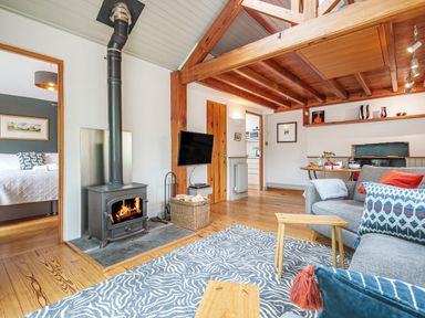 A living room with a wood burning stove a gray couch wooden ceiling beams and a patterned rug at The Stable At Oakbank in Elterwater