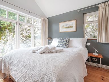A bedroom with a bed a pillow towels on the bed a bedside table with a lamp and large windows showing rock outside at The Stable At Oakbank in Elterwater