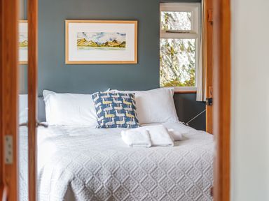A bedroom with a bed made with white linens and pillows and a framed landscape painting on the wall at The Stable At Oakbank in Elterwater