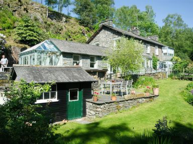 A garden with a stone patio table and chairs outside a stone house with a glass conservatory at The Stable At Oakbank in Elterwater