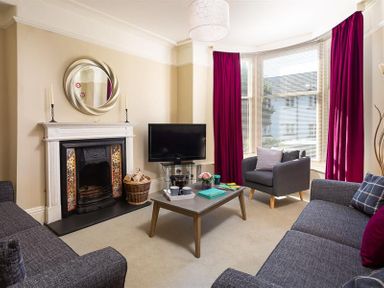A living room with a fireplace a television a coffee table two sofas and an armchair with red curtains at Highbank in Bowness