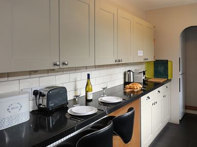 A kitchen countertop with toaster bread box wine bottle plates and chairs at Highbank in Bowness