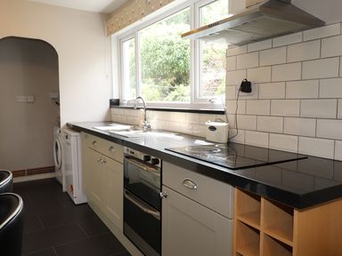 A kitchen with a black countertop oven stove sink washing machine and tiled backsplash at Highbank in Bowness