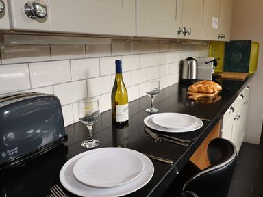 A kitchen countertop with two place settings wine bottle wine glasses toaster kettle and bread at Highbank in Bowness