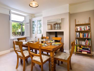 A dining room with a wooden table set for six near a window and a bookshelf at Highbank in Bowness