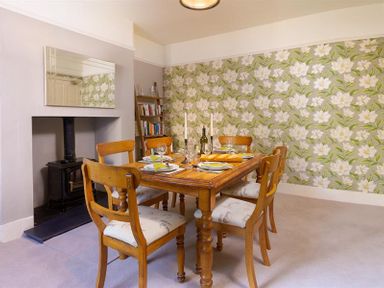 A dining room with a wooden table and six chairs near a fireplace and a bookshelf at Highbank in Bowness
