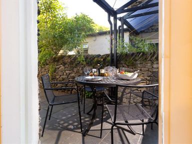 A patio area with a round metal table and four chairs under a pergola at Highbank in Bowness