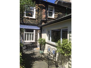 A small outdoor patio area with stone walls metal table and chairs a metal bench and potted plants at Highbank in Bowness
