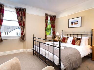 A bedroom with a metal bed frame two windows with patterned curtains and bedside tables at Highbank in Bowness