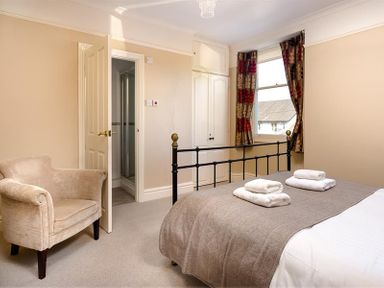 A bedroom with a bed covered with a brown blanket and two sets of folded white towels two doors beige armchair and window with patterned curtains at Highbank in Bowness