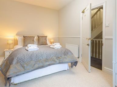 A bedroom with a double bed with gray and gold bedding two bedside tables with lamps and an open door showing a staircase at Highbank in Bowness