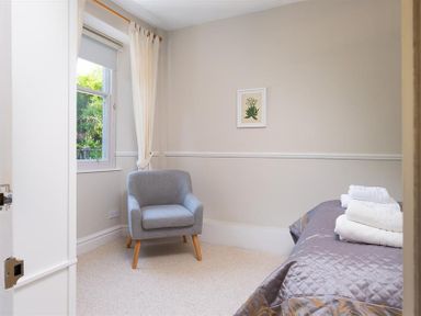 A small bedroom with a grey armchair near a window and a bed with towels on it at Highbank in Bowness