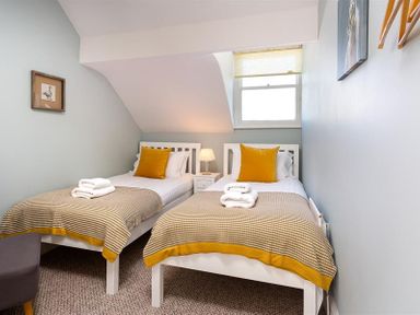 A bedroom with two single beds side by side with yellow pillows and blankets a lamp on a nightstand a window and framed pictures at Highbank in Bowness